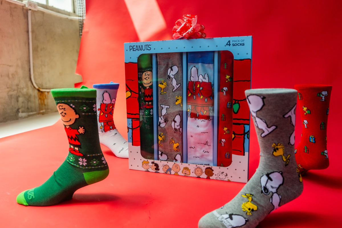 Peanuts-themed sock gift set with four colorful pairs featuring Snoopy and friends on a red background.