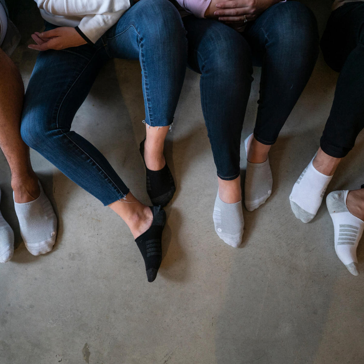 Basic no-show socks in black, gray, and white, worn with jeans on a concrete surface.