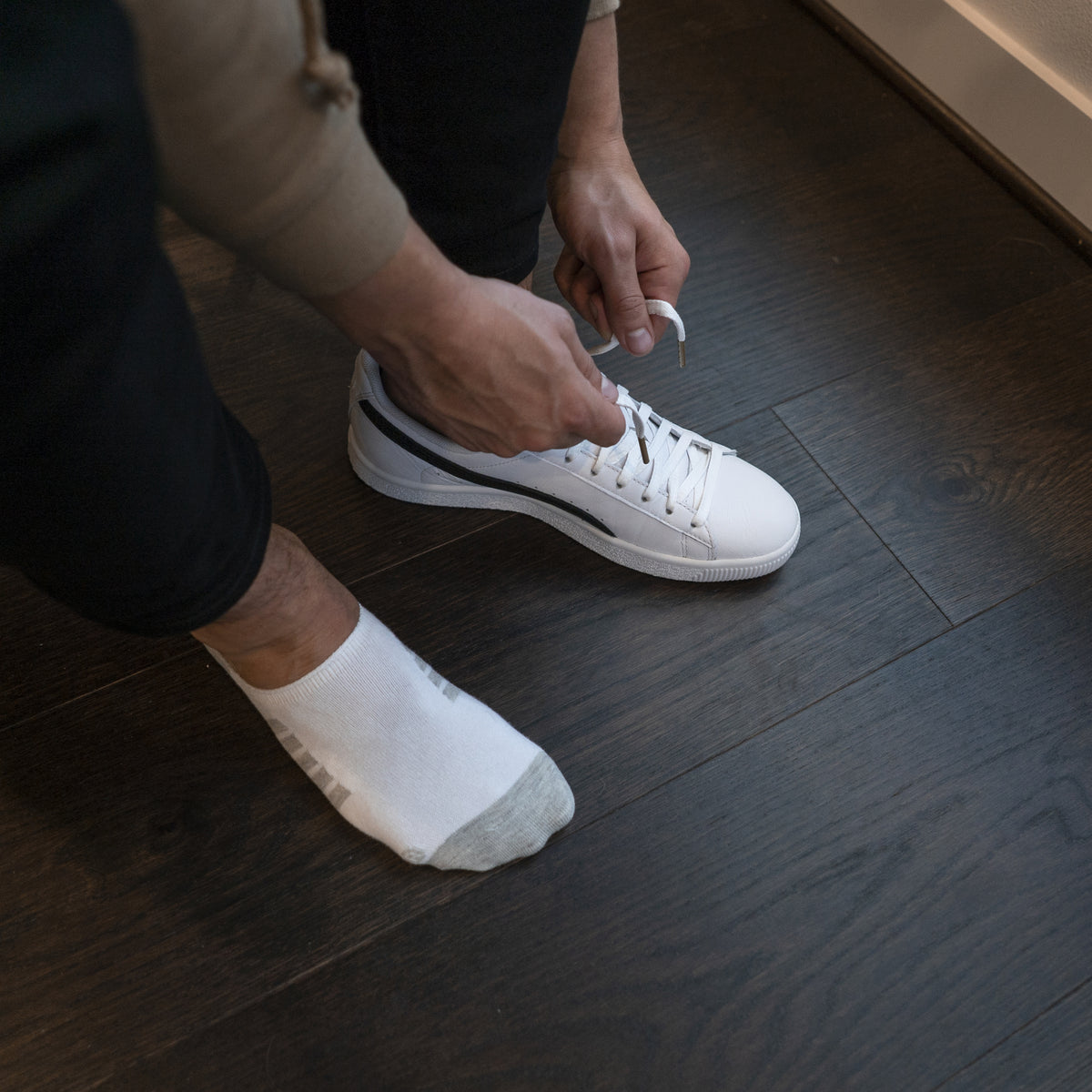 Basic no-show socks in white, worn with sneakers on a wooden floor.